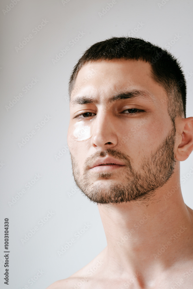 Obraz premium Man facial care skin rejuvenation face eye patches. Man facial care. Skin rejuvenation. Cosmetic product advertising. Satisfied caucasian guy applying collagen gel face eye patches on grey background.