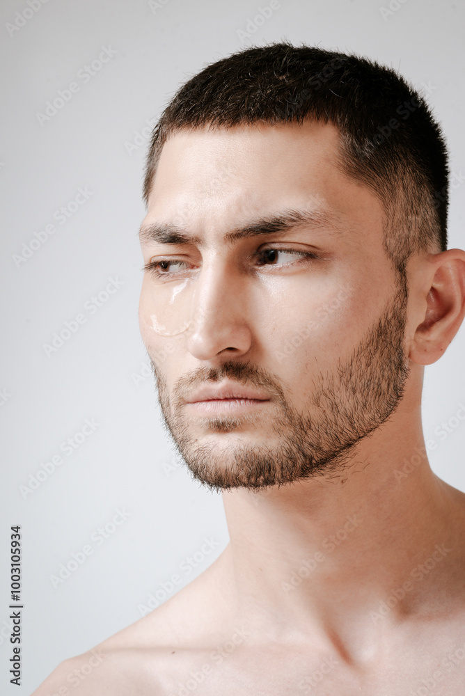 Man facial care skin rejuvenation face eye patches. Man facial care. Skin rejuvenation. Cosmetic product advertising. Satisfied caucasian guy applying collagen gel face eye patches on grey background. Man facial care skin rejuvenation face eye patches. Man facial care. Skin rejuvenation. Cosmetic product advertising. Satisfied caucasian guy applying collagen gel face eye patches on grey background.