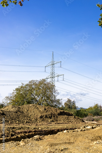 eine unbefestigte Straße mit einem großen Haufen Erde in der Mitte, Strommasten, Stromkabel, elektrische Kabel, Maschinen und Drähte, Stromleitungen