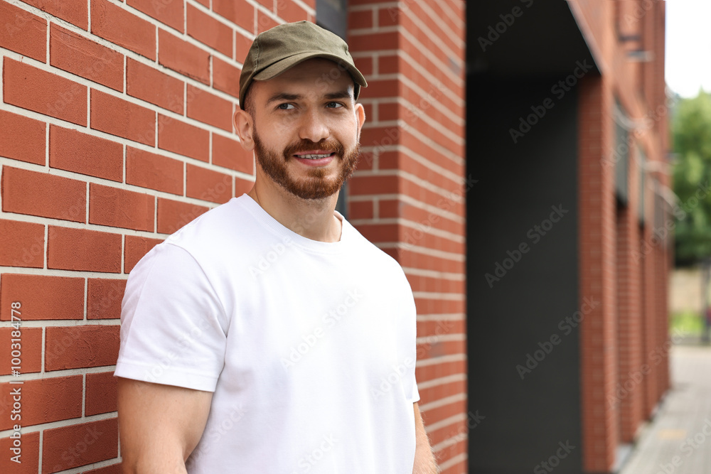 Fototapeta premium Portrait of smiling man in baseball cap near building outdoors. Space for text