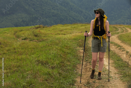 Young hiker with backpack and trekking poles in mountains, space for text