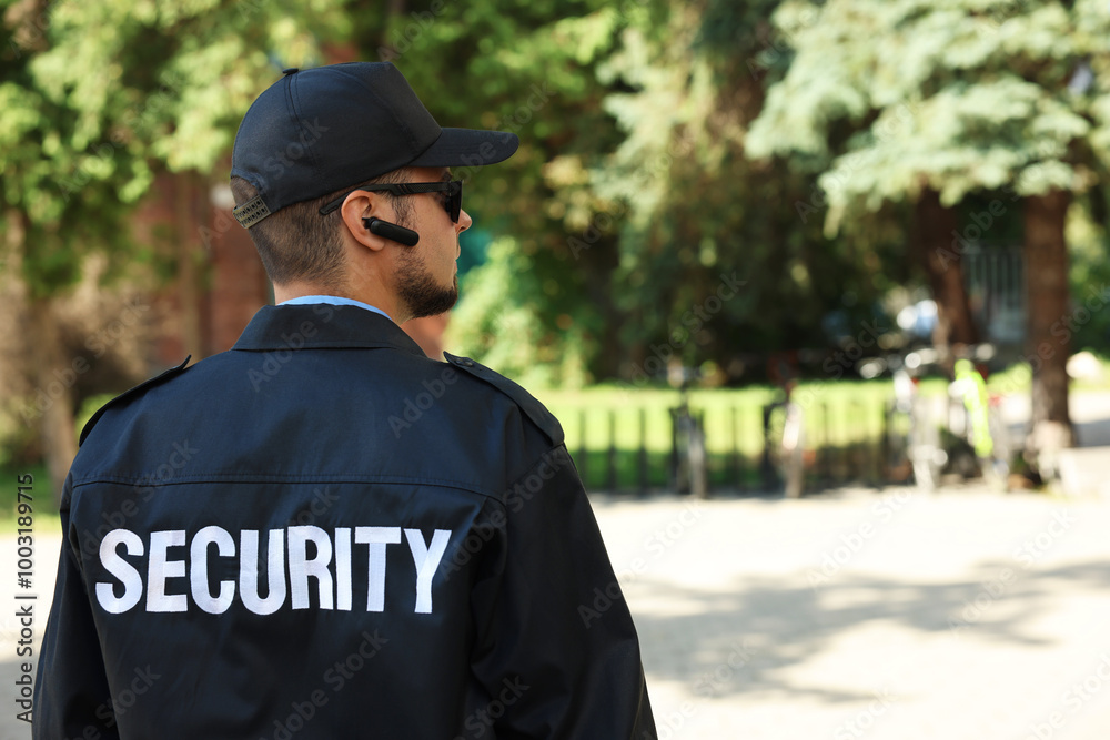 Obraz premium Security guard in uniform and sunglasses outdoors, back view. Space for text
