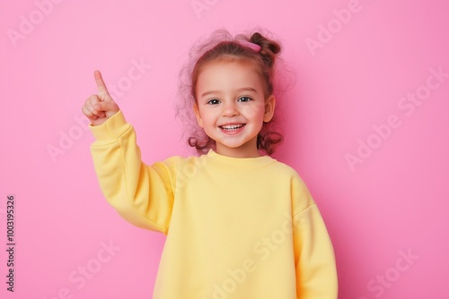 smiling little girl wearing casual bright clothes with pointing up gesture and copy space, solid color background