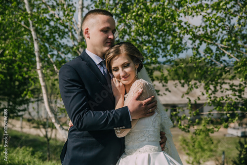 A woman is getting ready for her wedding and is looking at herself in a mirror. She is wearing a white dress and has her hair in a bun. The mirror is placed on a dresser