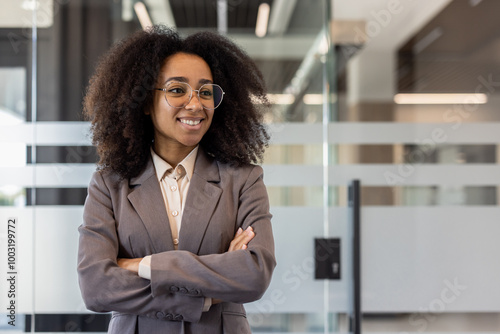 Smiling young African American businesswoman in suit standing in office, arms crossed on chest, looking away Free Download Smiling young African American businesswoman in suit standing in office, arms crossed on chest, looking away - GFXLoad