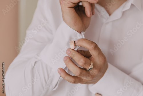 A man is getting ready for a formal event and is putting on a gold ring and cufflinks