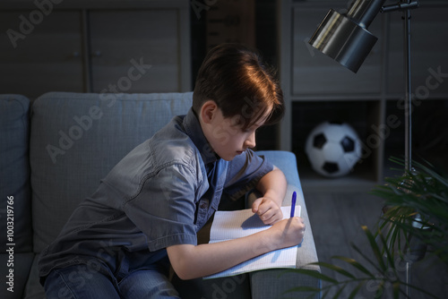 Little boy sitting on sofa and doing homework at home in evening