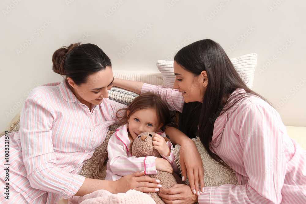 Young lesbian couple and adopted little girl with toy lying in bedroom Young lesbian couple and adopted little girl with toy lying in bedroom