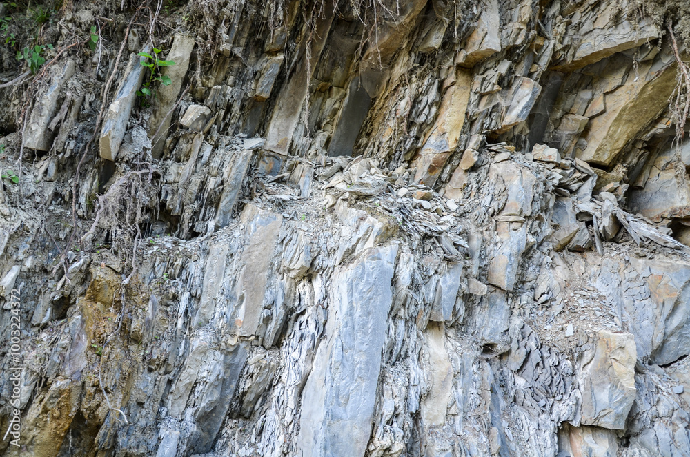 Grey rocky cliff face with visible layers and strata indicating geological processes, showcasing various sizes and shapes of stones and boulders. Texture typical of sedimentary rock formations Grey rocky cliff face with visible layers and strata indicating geological processes, showcasing various sizes and shapes of stones and boulders. Texture typical of sedimentary rock formations