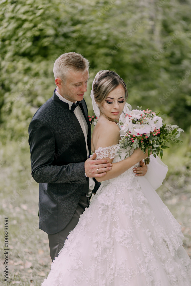 A bride and groom are posing for a picture in a forest. The bride is holding a bouquet of flowers A bride and groom are posing for a picture in a forest. The bride is holding a bouquet of flowers