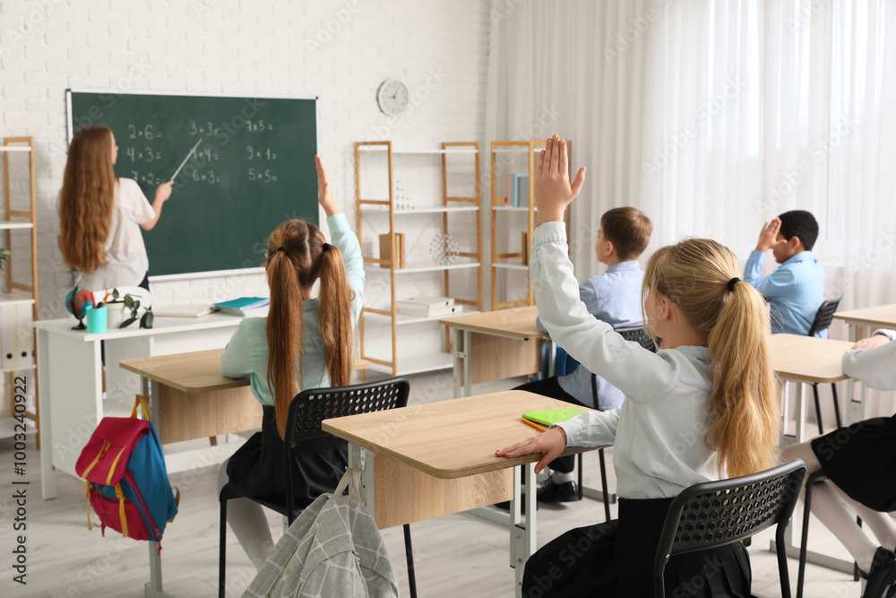 Group of children with raised hands during lesson in classroom