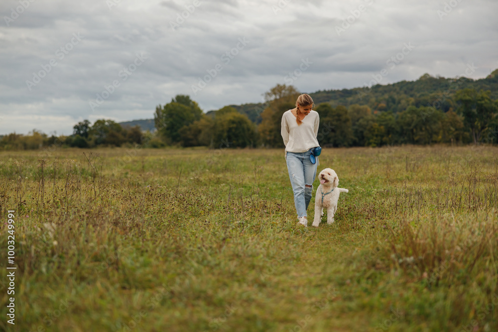 A woman leisurely strolls with her dog in a tranquil field, beautifully surrounded by the wonders of nature A woman leisurely strolls with her dog in a tranquil field, beautifully surrounded by the wonders of nature