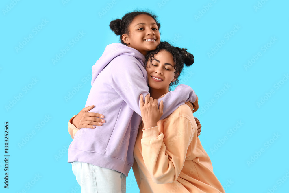 Happy young African-American woman with her daughter hugging on blue background Happy young African-American woman with her daughter hugging on blue background