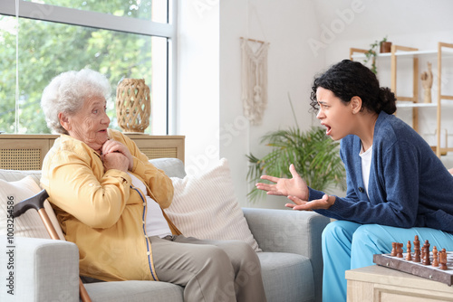 Young African-American female medical worker shouting at elderly woman in nursing home