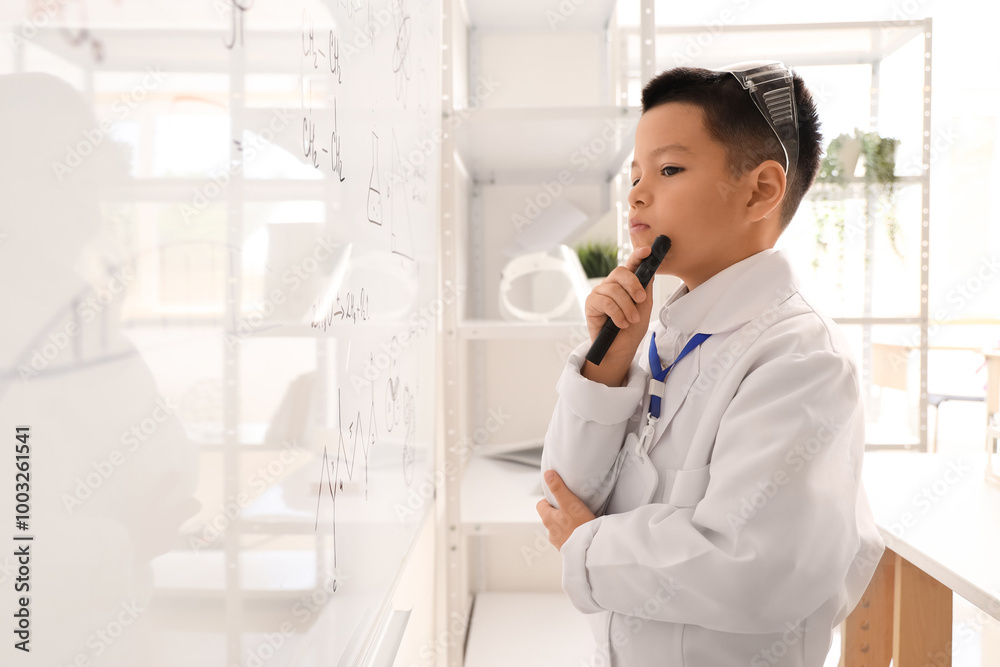 Thoughtful little boy near whiteboard in chemistry classroom Thoughtful little boy near whiteboard in chemistry classroom