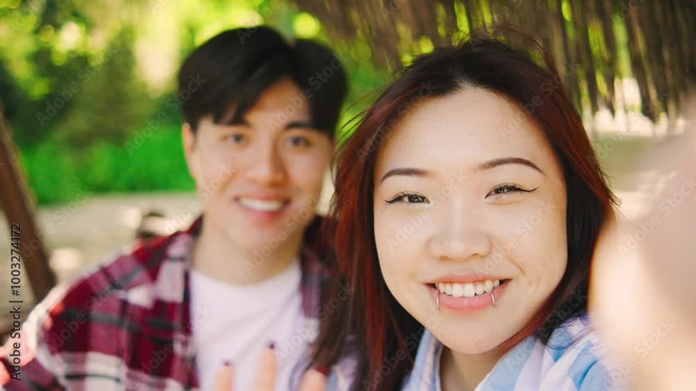 POV Happy asian couple takes a selfie as they swing together in a lush green park, joyfully capturing fun moments under the bright, warm summer sun POV Happy asian couple takes a selfie as they swing together in a lush green park, joyfully capturing fun moments under the bright, warm summer sun
