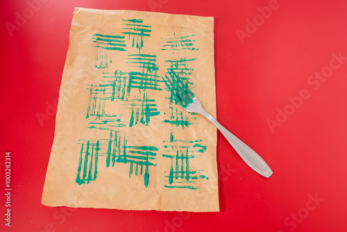 a sheet of brown paper with green paint patterns created by the tines of a fork, top view, red background photo