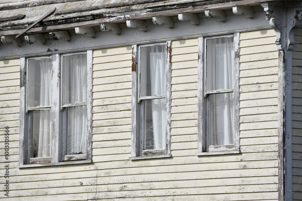 Fototapeta premium Victorian house, line of windows, faded yellow paint, peeling siding.