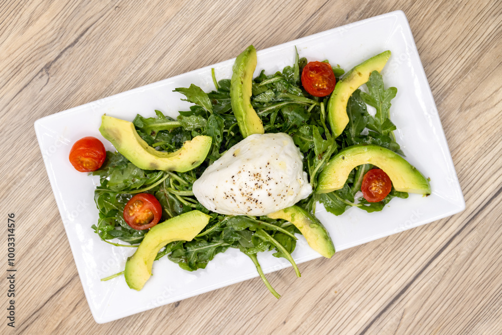 Overhead view of Italian herb dressing over mozzarella cheese, avocado, cherry tomato, and arugula salad Overhead view of Italian herb dressing over mozzarella cheese, avocado, cherry tomato, and arugula salad