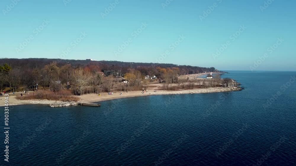 Aerial push-in drone shot over the blue waters of Lake Ontario. Aircraft is slowly approaching the shore full of people playing and walking around, enjoying a lovely morning Winter day. Aerial push-in drone shot over the blue waters of Lake Ontario. Aircraft is slowly approaching the shore full of people playing and walking around, enjoying a lovely morning Winter day.