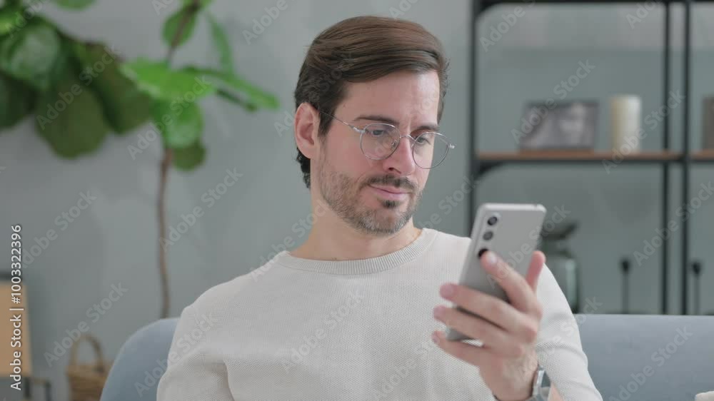 Portrait of Young Man Text Messaging on Phone Sitting on Sofa at Home Portrait of Young Man Text Messaging on Phone Sitting on Sofa at Home