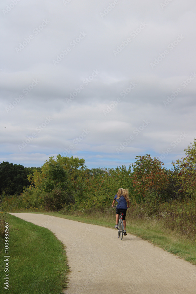 Woman with long red hair riding a bicycle on the Des Plaines River Trail in autumn at Old School Forest Preserve in Libertyville, Illinois Woman with long red hair riding a bicycle on the Des Plaines River Trail in autumn at Old School Forest Preserve in Libertyville, Illinois