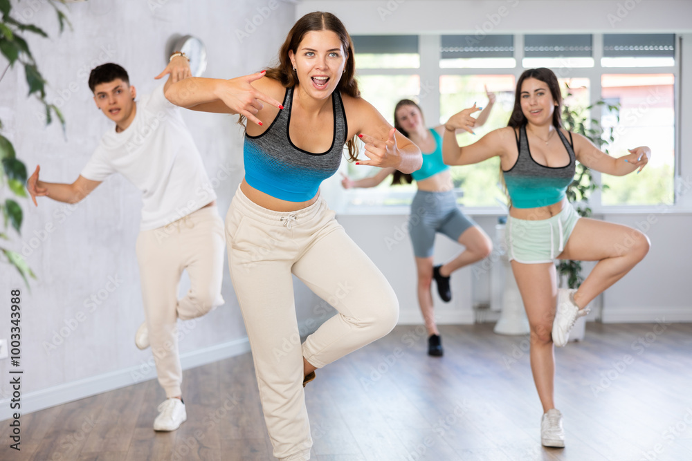 Obraz premium Cheerful expressive young girl practicing hip-hop movements during group dance class in studio..