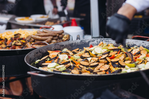 Food festival with street food stall kiosk, open-air outdoor fair market, assortment of different fried grilled barbecued vegetables, pepper, eggplant, zucchini, aubergine, cabbage on a large pan photo