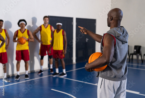 Coach holding basketball and instructing team of players during practice session