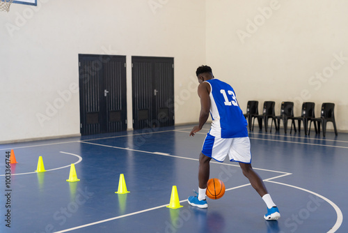 Dribbling basketball, athlete practicing agility drills with cones in gymnasium, copy space