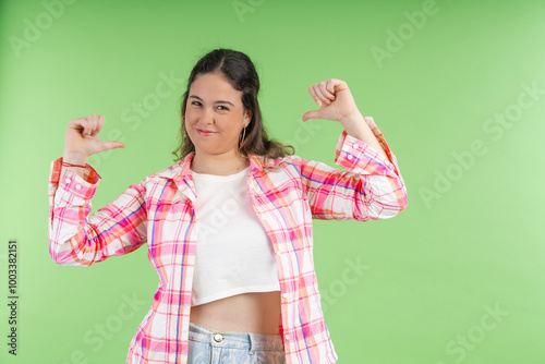 Young woman pointing her thumbs at herself with a proud expression on green background photo