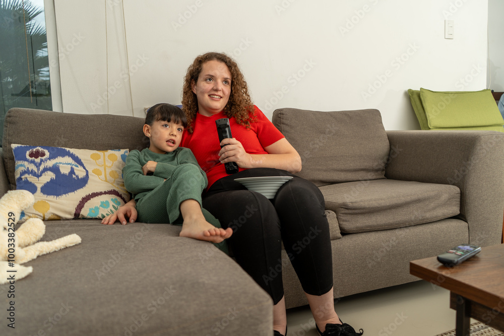 mother and daughter concentrated watching tv together and eating popcorn in the living room looking television mother and daughter concentrated watching tv together and eating popcorn in the living room looking television