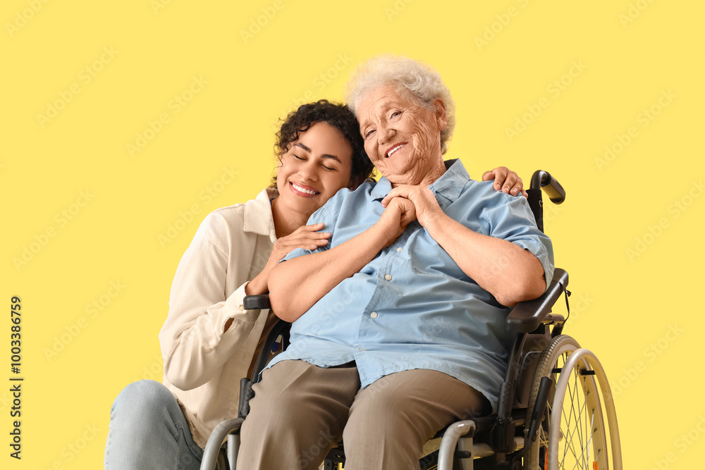 Young African-American female medical worker with elderly woman on wheelchair against yellow background Young African-American female medical worker with elderly woman on wheelchair against yellow background