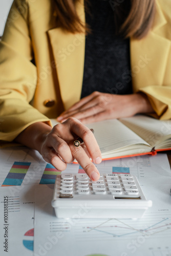 Close-up of a businesswoman using a calculator and reviewing financial charts and graphs at a desk.