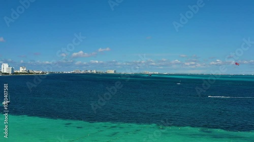 A dynamic view of various watersports over the ocean, featuring jet skis, a sailboat, and parasailing activities, capturing the excitement and adventure of a vibrant seaside experience.