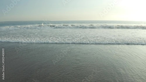 A serene view of a young woman standing on the beach, facing the ocean as gentle waves approach her, capturing a peaceful moment of reflection and connection with nature.
