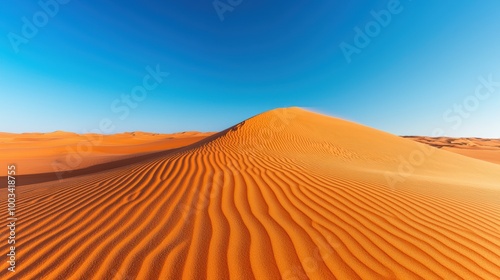 Vast orange sand dune under clear blue sky, natural desert scenery.