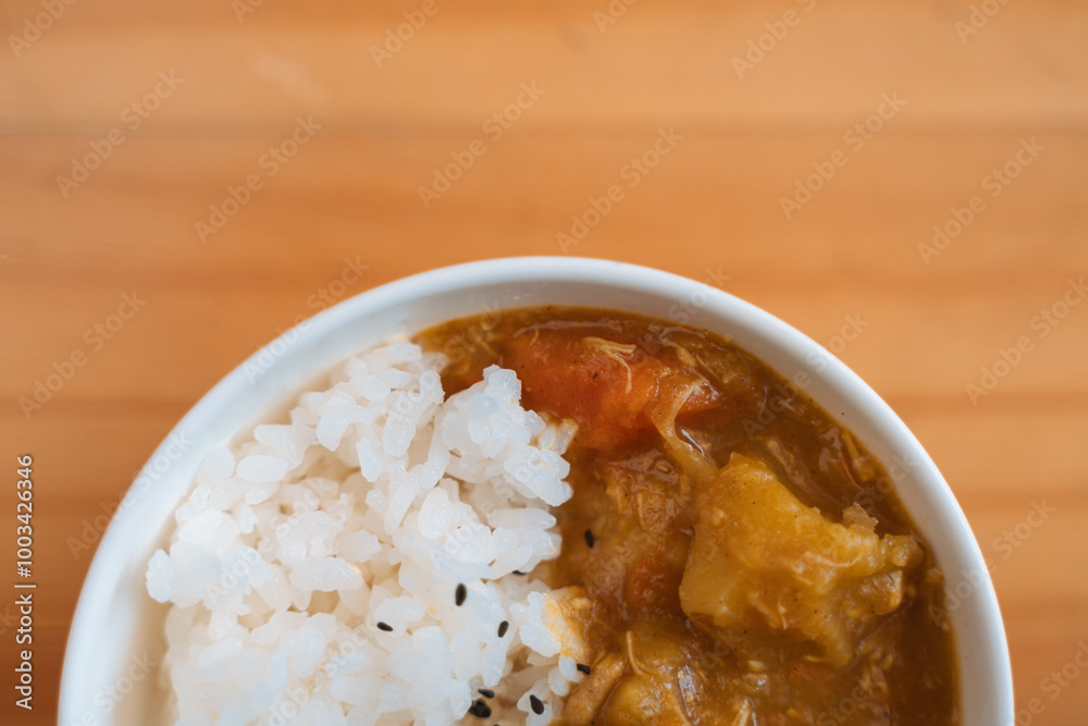 White rice with black sesame seeds and vegetable curry in a bowl on a wooden surface. White rice with black sesame seeds and vegetable curry in a bowl on a wooden surface.