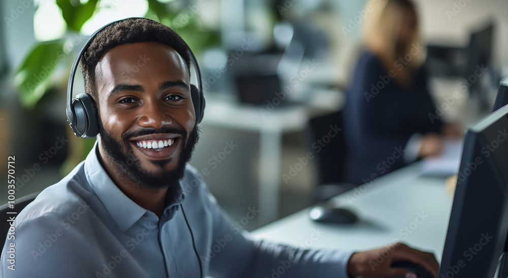 Cool worker smiling at the camera in a busy office using headset Cool worker smiling at the camera in a busy office using headset