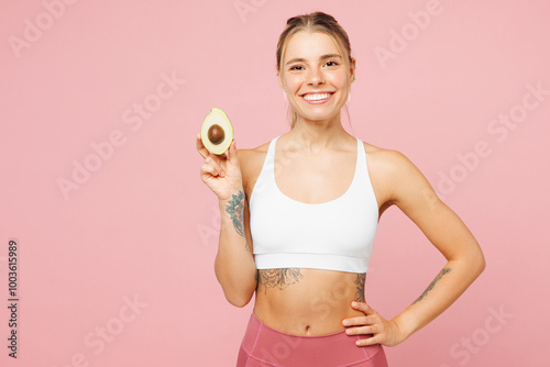 Young smiling happy fun woman wears white top casual clothes hold in hand half of avocado isolated on plain pastel light pink background. Proper nutrition healthy fast food unhealthy choice concept.