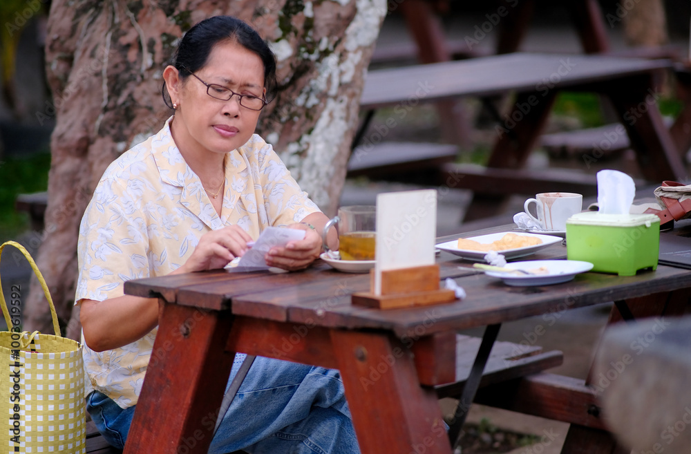 Fototapeta premium Woman sitting on a wooden bench in a garden restaurant, enjoying her afternoon ginger tea