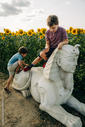 Children playing on a sphinx statue in a sunflower field photo