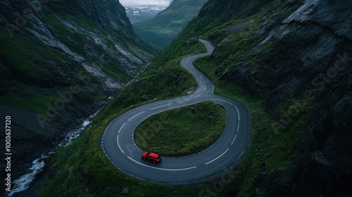 A winding road snakes through a lush valley, with a red car prominently positioned, showcasing the beauty of nature and scenic driving.