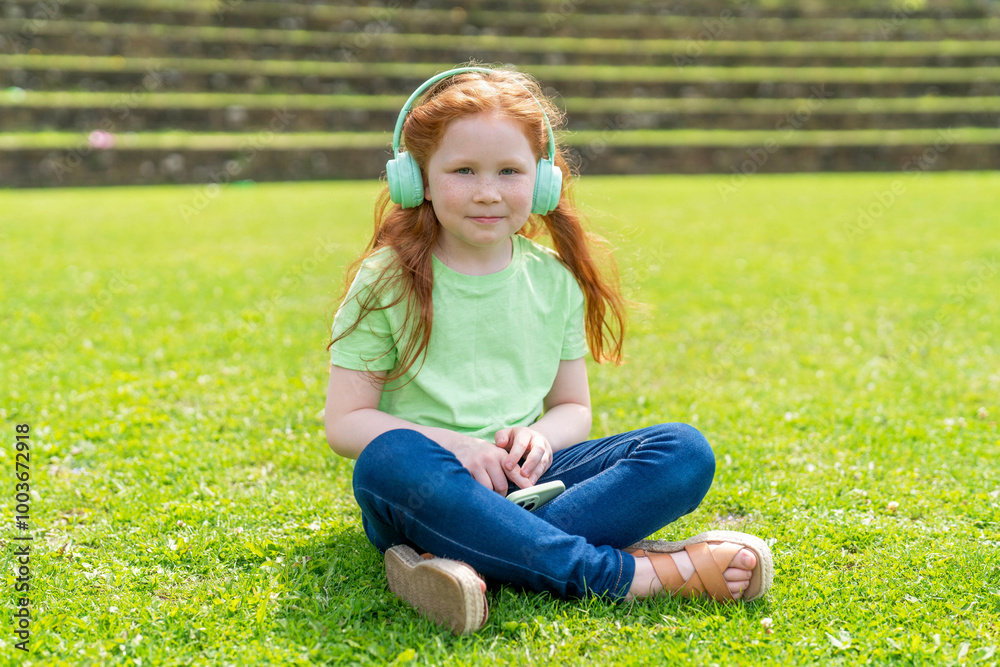 A young girl with headphones enjoys a peaceful moment on the green lawn during a sunny day in the park A young girl with headphones enjoys a peaceful moment on the green lawn during a sunny day in the park