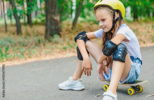 Cute little girl child sitting on skateboard in park, wearing a white t-shirt and sneakers photo