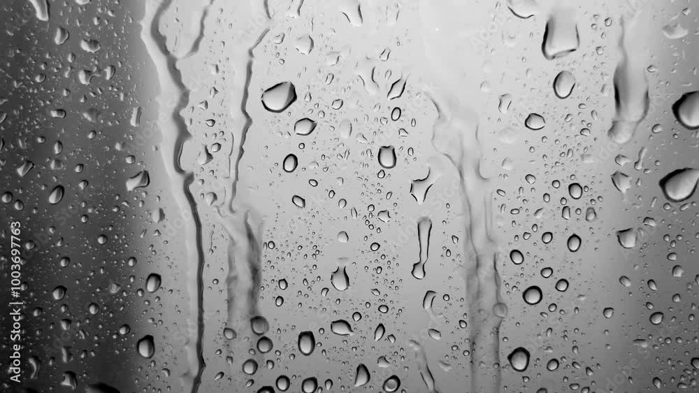 Raindrops falling down the window glass. Abstract background of raindrops in gray tones