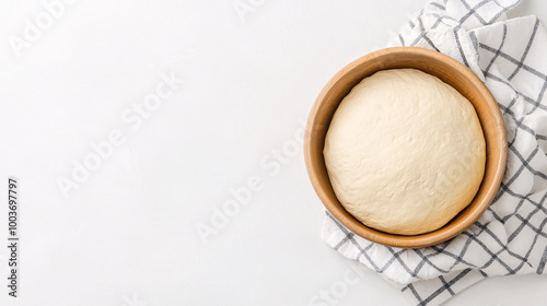 A round dough rising in a wooden bowl on a white checkered kitchen towel. White background with copy space. Baking concept.