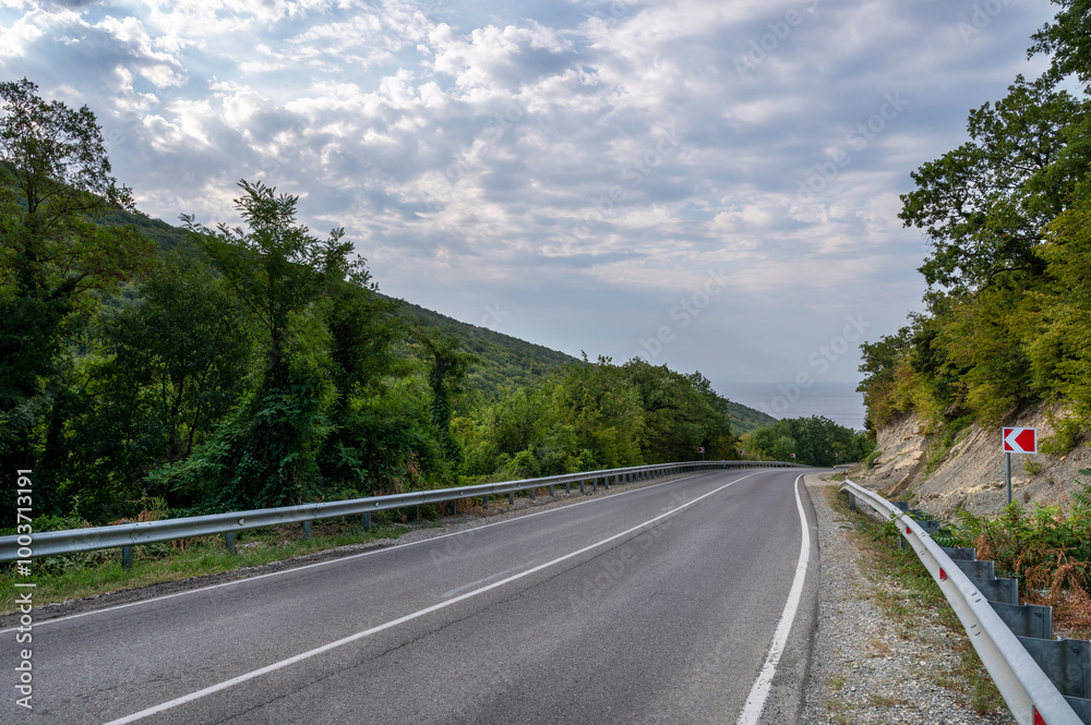 Road landscape forest, mountains and sea on the horizon. Empty long mountain road to the horizon on a sunny summer day with dramatic cloudy sky. Highway turn panoramic view. Road landscape forest, mountains and sea on the horizon. Empty long mountain road to the horizon on a sunny summer day with dramatic cloudy sky. Highway turn panoramic view.