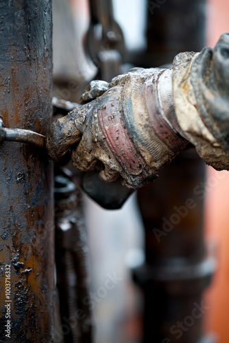 An oil field worker uses a wrench to tighten equipment at a drilling site, showcasing the skill and effort involved in oil extraction during late afternoon hours.