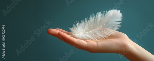 A delicate white feather resting on an open hand against a soft teal background, symbolizing lightness and tranquility.